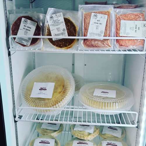 A refrigerator shelf displaying various packaged meats and prepared foods in clear containers.