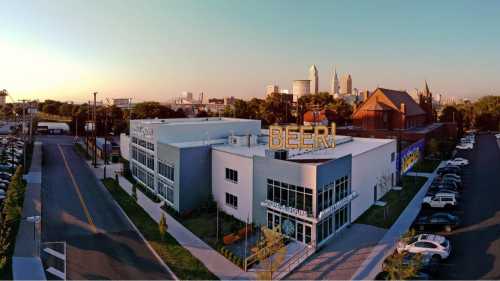 A modern building with a large "BEER!" sign, set against a city skyline at sunset.