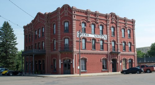 Historic red brick building with multiple windows, featuring a sign that reads "Grand Union," set in a small town.