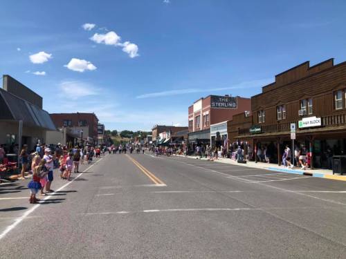 A bustling main street lined with shops, people gathered for an event under a clear blue sky with a few clouds.