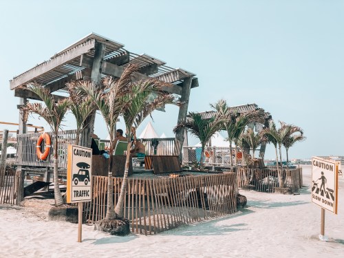 Beach scene with wooden structures, palm trees, and caution signs for traffic and safety.