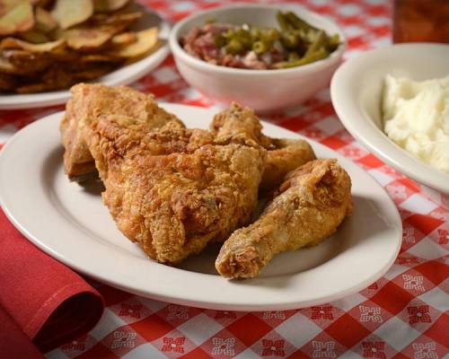A plate of crispy fried chicken with sides of mashed potatoes, green beans, and potato slices on a checkered tablecloth.