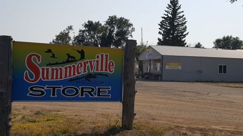 A colorful sign for "Summerville Store" in front of a small building surrounded by trees and a dirt road.