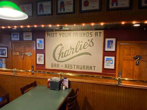 A cozy restaurant interior featuring a sign that reads "Meet Your Friends at Charlie's Bar-Restaurant" on the wall.