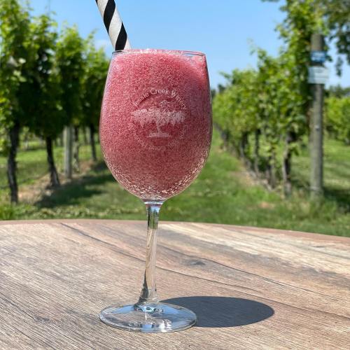 A frosty pink drink in a wine glass with a striped straw, set against a vineyard backdrop.