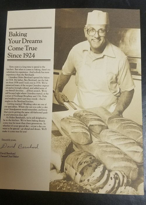 A smiling baker in a chef's hat stands with freshly baked loaves of bread, promoting a bakery's legacy since 1924.
