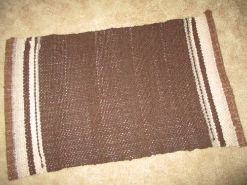 A woven brown rug with light and dark stripes along the edges, placed on a beige carpet.