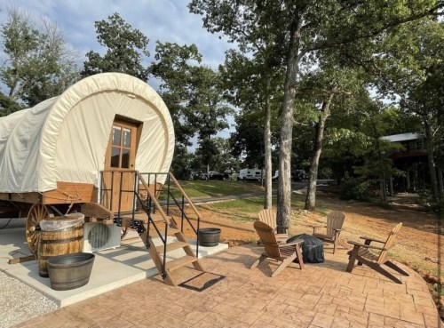 A cozy outdoor seating area with wooden chairs near a vintage-style wagon surrounded by trees.
