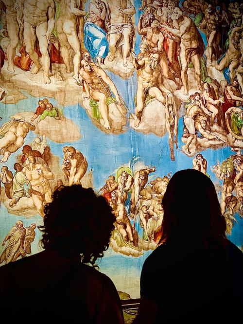 Two people silhouetted in front of a vibrant mural depicting biblical scenes and figures.