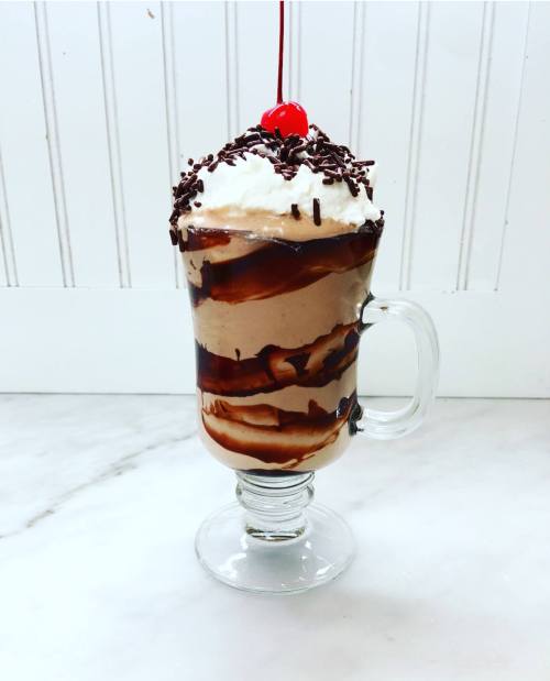 A tall glass dessert with layers of chocolate ice cream, whipped cream, chocolate syrup, and a cherry on top.
