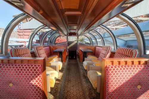 Interior of a vintage train car featuring plush seating and large windows, showcasing a warm, inviting atmosphere.