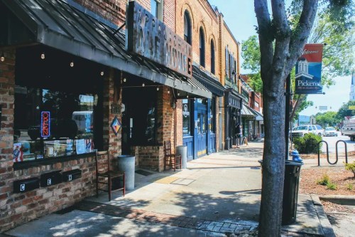 A charming street view of brick storefronts with outdoor seating and a welcoming sign for Pickens.
