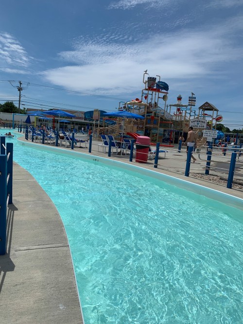 A winding lazy river pool with clear water, surrounded by blue railings and a water park in the background.
