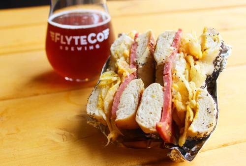A sandwich with layers of meat and mustard, served with a glass of amber beer on a wooden table.