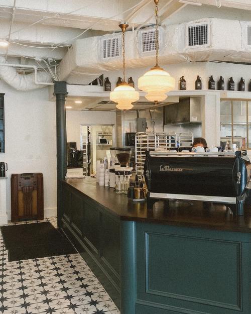 A stylish café interior featuring a dark wooden counter, vintage lighting, and patterned tile flooring.