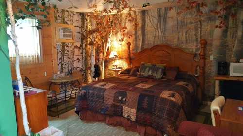 Cozy bedroom with a wooden bed, forest-themed decor, and a small dining area surrounded by nature-inspired wallpaper.