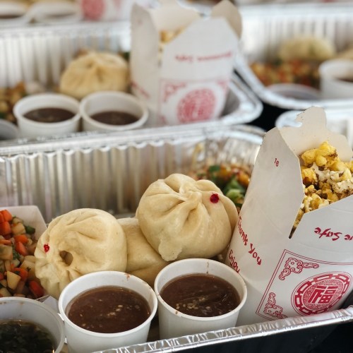 A variety of food containers featuring steamed buns, dipping sauces, and a side of popcorn and salad.