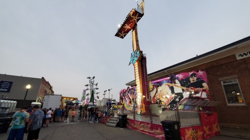 A vibrant carnival scene with rides, colorful decorations, and a crowd enjoying the festivities in the evening light.