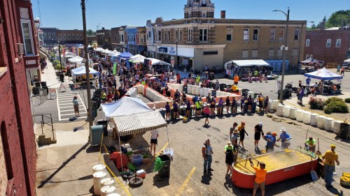 A bustling street festival with tents, vendors, and a crowd enjoying activities under a clear blue sky.