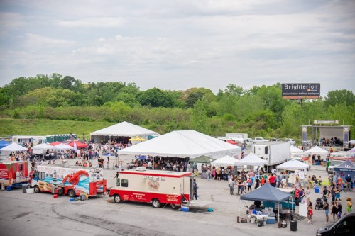 A bustling outdoor event with food trucks, tents, and a crowd enjoying activities under a cloudy sky.