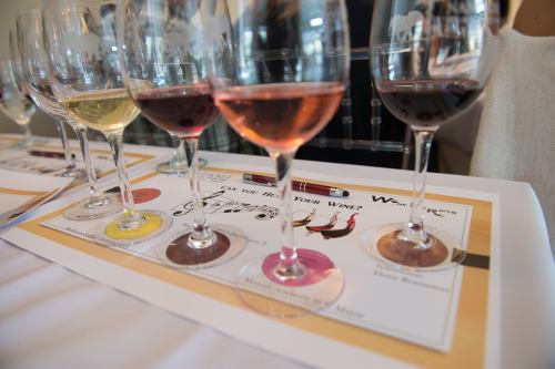 A row of wine glasses with different colored wines on a tasting sheet at a wine tasting event.
