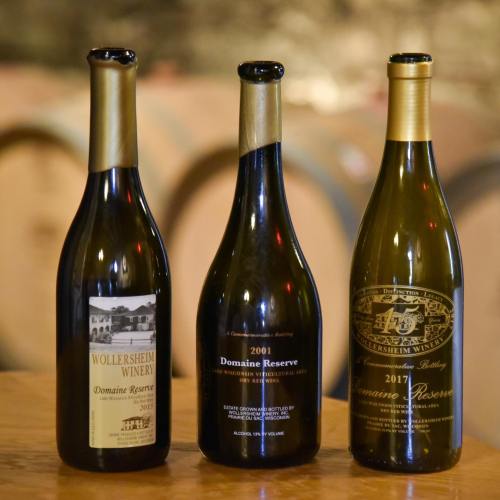 Three wine bottles on a wooden table, featuring labels for Wollersheim Winery and Domaine Reserve from 2001 and 2017.