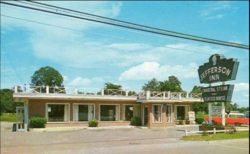 A vintage roadside inn with a sign reading "Jefferson Inn," featuring a steak and seafood house, surrounded by greenery.