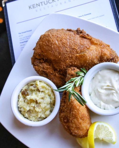 A plate of crispy fried chicken with sides of mashed potatoes and dipping sauce, garnished with a lemon slice and herbs.