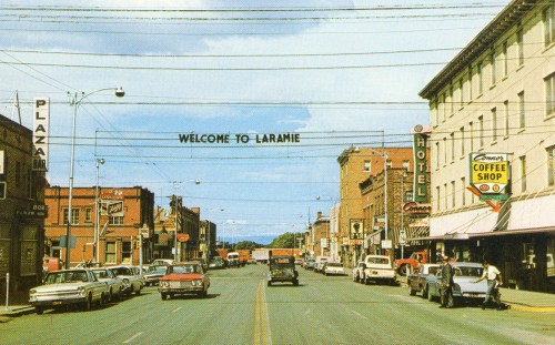 A vintage street view of Laramie, featuring shops, cars, and a "Welcome to Laramie" sign overhead.