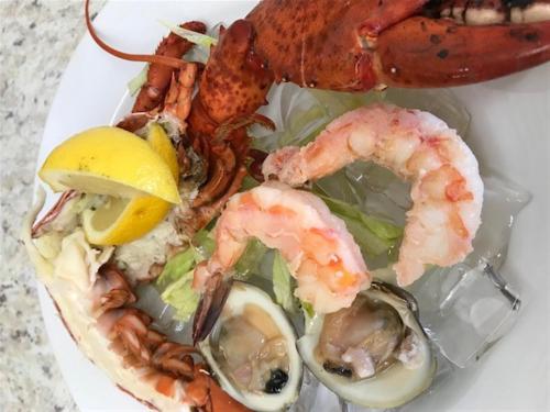 A plate of seafood featuring lobster, shrimp, and oysters garnished with lemon and lettuce.