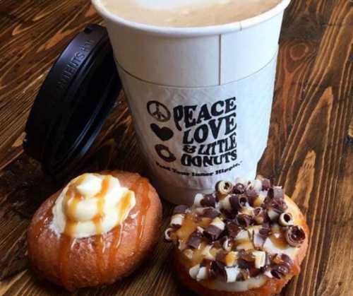 A cup of coffee next to two donuts, one with caramel and cream, the other topped with chocolate curls.