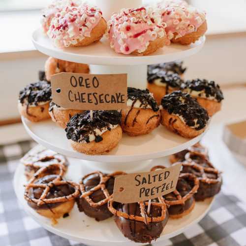 A tiered stand displays various donuts, including Oreo cheesecake and salted pretzel, with labels for each flavor.