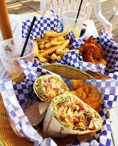 A basket of food featuring a wrap, chips, crinkle fries, and fried chicken, all served in checkered paper.