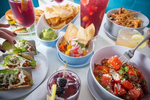 A vibrant spread of colorful dishes, including tacos, guacamole, chips, and drinks, arranged on a table.