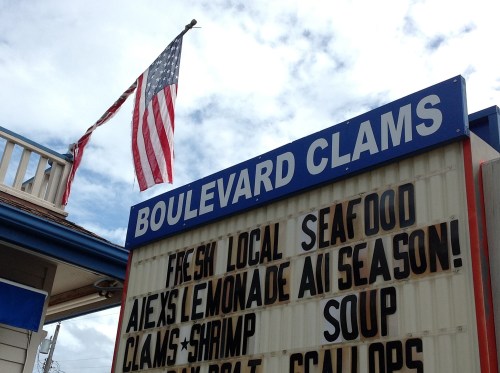 Sign for Boulevard Clams featuring fresh seafood, lemonade, and a flag waving in the background.