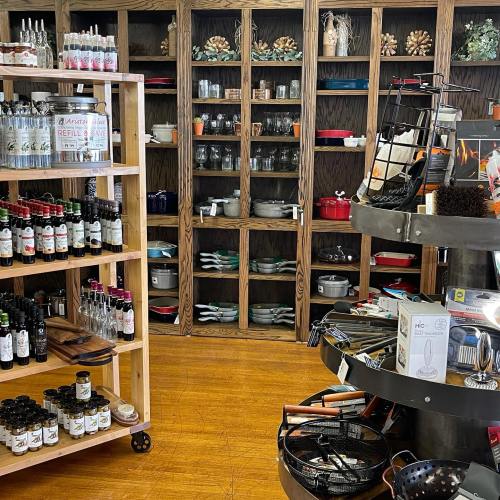 A cozy kitchenware store featuring shelves of pots, pans, and various cooking supplies, with displays of oils and spices.