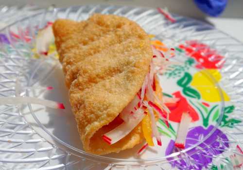 A crispy taco filled with colorful vegetables, served on a decorative plate with floral patterns.