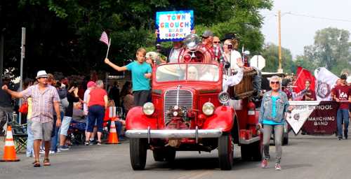 A vintage fire truck in a parade, with people waving and holding signs, surrounded by a cheering crowd.