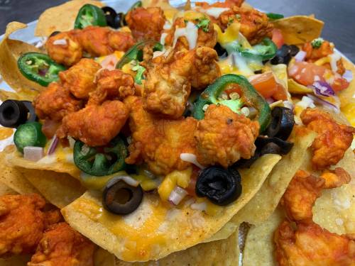 A close-up of nachos topped with spicy chicken, jalapeños, olives, tomatoes, and melted cheese.