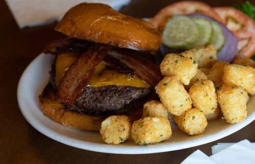 A juicy cheeseburger with bacon on a bun, served with crispy tater tots and fresh tomato, onion, and pickle slices.
