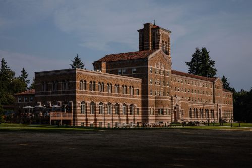Historic brick building with a tower, surrounded by trees and a grassy area, under a clear blue sky.