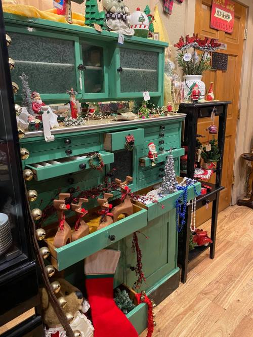 A festive green cabinet filled with holiday decorations, including Santa figures, reindeer, and colorful ornaments.