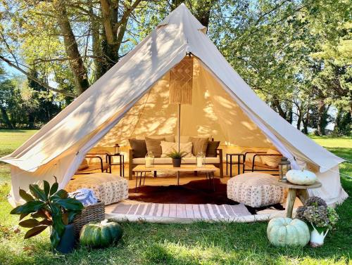 A cozy glamping tent with seating, cushions, and decorative pumpkins, set in a sunny outdoor area surrounded by trees.