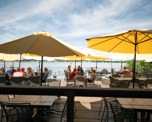 Outdoor dining area with yellow umbrellas, people enjoying meals by the water on a sunny day.