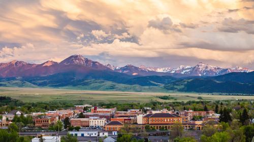 A scenic view of a town surrounded by mountains under a colorful sky at sunset.