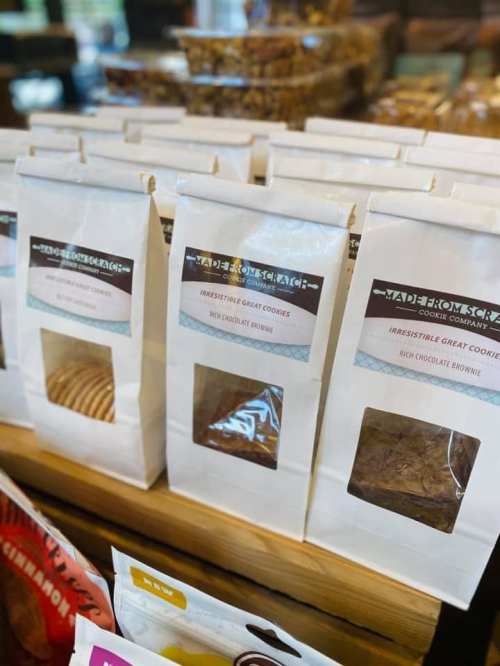 A display of cookie packages on a wooden shelf, featuring various flavors and clear windows to see the cookies inside.