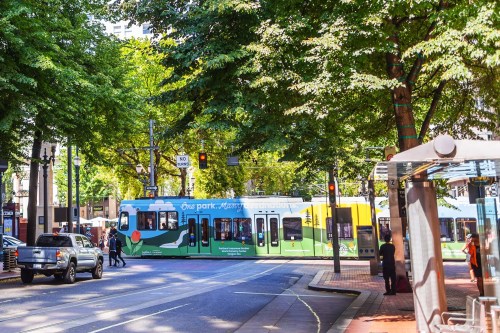 A colorful tram travels down a tree-lined street, with pedestrians and vehicles nearby.