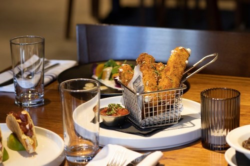 A basket of crispy fried food sits on a wooden table, accompanied by dipping sauce and other dishes.