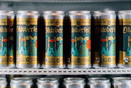 Cans of Oktoberfest beer lined up on a shelf, featuring colorful designs and festive graphics.