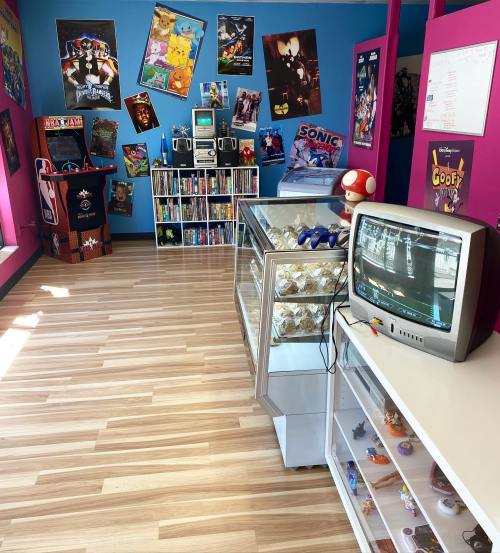 A colorful game room with retro decor, shelves of games, a vintage TV, and arcade machines.